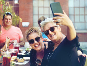 One man and two women at a restaurant table laughing and taking a selfie.